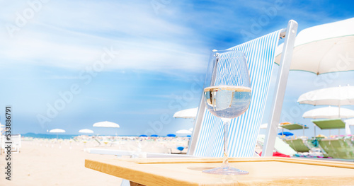 A glass of white wine on the beach. Blue sky, skyline and sunny day. Resort deluxe beach holiday. Place for text. Copy space. High quality photo