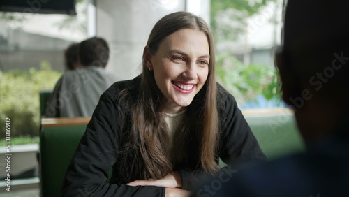 Happy Young woman sitting at coffee shop table in conversation with friend. Smiling person at cafe place laughing