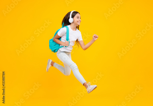 Schoolgirl with backpack hold aplle ready to learn. School children with school bag on isolated yellow studio background. Excited teenager, jump and run, jumping child. © Olena