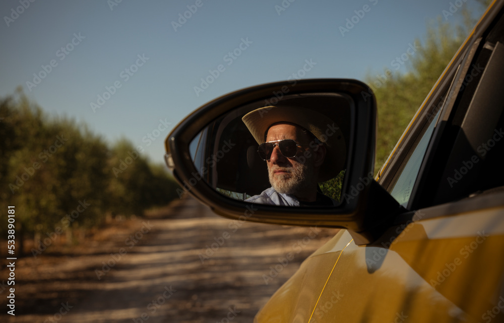 Adult man in cowboy hat driving car in olive grove, Almeria, Spain