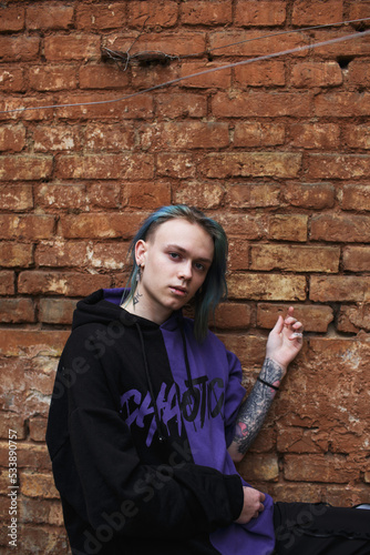 Portrait of a young tattooed punk guy with long dyed hair. A guy with blue hair is standing on the street . Stylish modern youth