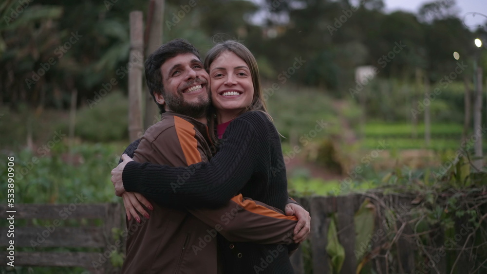 Fototapeta premium Couple in 30s embrace standing outdoors at dusk evening wearing sweaters during cold night. Friends hugging each other