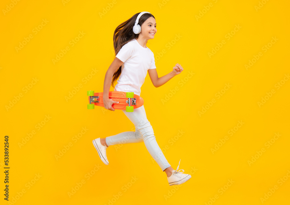 Happy teenager portrait. Jump and run. Fashion teenage lifestyle, beautiful teen girl with skateboard and headphones isolated on studio background. Smiling girl.
