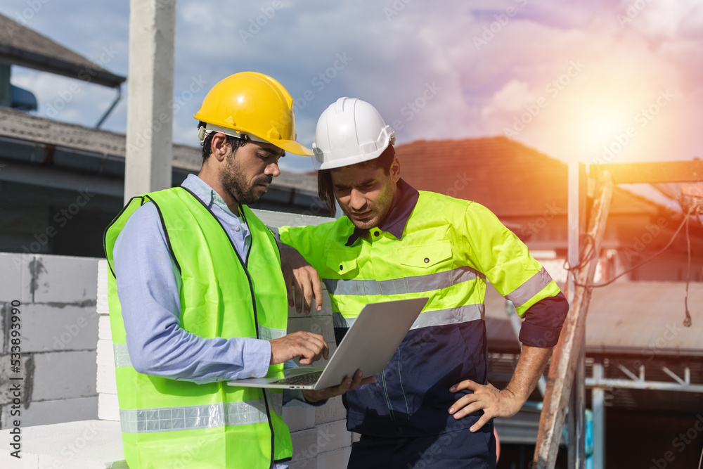 Professional construction engineer team, Two man engineer wear uniform holding laptop standing at construction site. Workers supervise the construction of the building. Professional construction engineer team, Two man engineer wear uniform holding laptop standing at construction site. Workers supervise the construction of the building.