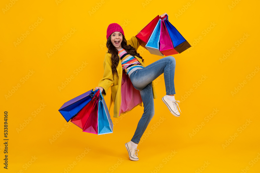 Beautiful fashion teenager child girl with shopping bags on yellow background. Shopaholic shopping and fashion. Run and jump. Kid with shopping sale bags. Autumn shopping sale. Beautiful fashion teenager child girl with shopping bags on yellow background. Shopaholic shopping and fashion. Run and jump. Kid with shopping sale bags. Autumn shopping sale.