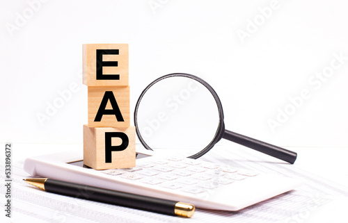 On a white calculator, next to a magnifying glass and a black pen, wooden cubes marked EAP Employee Assistance Program stand upright.