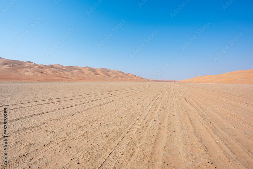 Track in the desert going thru a sabkha with blue sky and copy space.  Middle East, Arabian Peninsula 