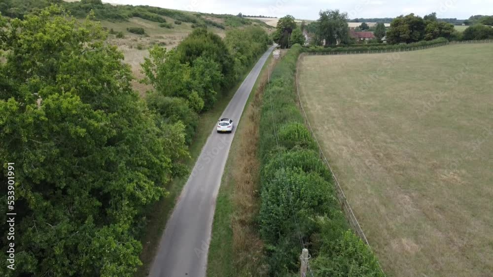 Long white car driving fast down a long country road in the south of england during a cloudy day in the summertime Long white car driving fast down a long country road in the south of england during a cloudy day in the summertime