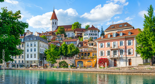 A panoramic view of the embankment of the Swiss city of Thun, the ancient architecture of the city, decorated with flowers and trees, is reflected in the transparent azure river Aare