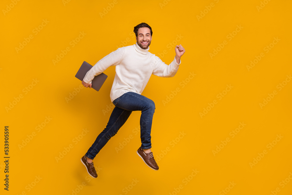 Photo of energetic active programmer guy jump run carry pc device wear white sweater jeans isolated yellow color background