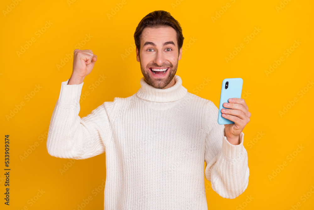 Photo of crazy guy hold telephone raise fist rejoice glad post comment wear white sweater isolated yellow color background Photo of crazy guy hold telephone raise fist rejoice glad post comment wear white sweater isolated yellow color background