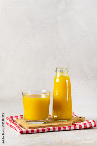 Fototapeta Naklejka Na Ścianę i Meble -  Bottles of Juice for Healthy Diet Autumn Pumpkin Juice in Bottle and Glass Wooden Tray Gray Background Vertical