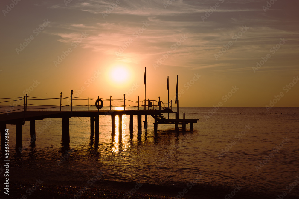 Silhouette of a wooden sea pier against the background of the rising sun. Seascape with the rising sun. Sunrise on the sea.