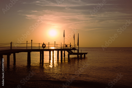 Silhouette of a wooden sea pier against the background of the rising sun. Seascape with the rising sun. Sunrise on the sea. © Galina