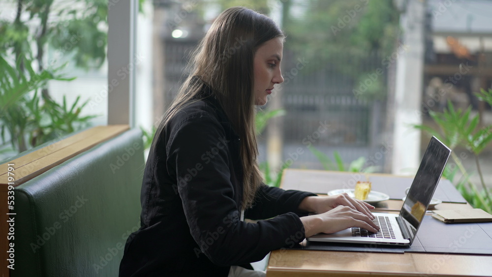 Young woman opening laptop seated at coffee shop by window overlooking city street. Person using computer at cafe restaurant browsing internet Young woman opening laptop seated at coffee shop by window overlooking city street. Person using computer at cafe restaurant browsing internet