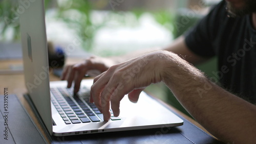 Young man browsing internet using laptop seated at coffee shop. Person looking at computer screen typing on keyboard searching online