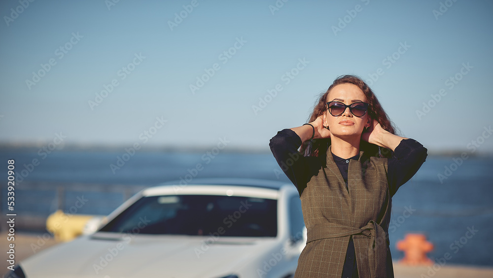 beautiful business woman in sunglasses and business suit at sunset on the background of an expensive car. beautiful business woman in sunglasses and business suit at sunset on the background of an expensive car.