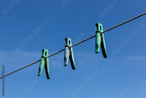 Three plastic clothespins hanging on a clothesline against a blue sky.