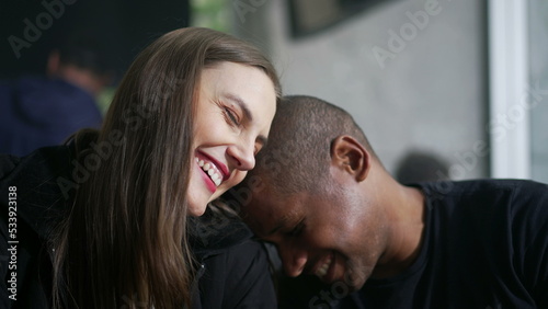 Romantic diverse couple laughing and smiling. A black man leaning on white girl shoulder showing love and affection © Marco