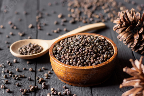 Black pepper seeds placed in a wooden cup are placed on an old black wooden table.
