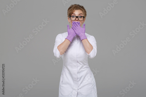 Woman doctor in white coat emotionally surprised isolated on gray background.