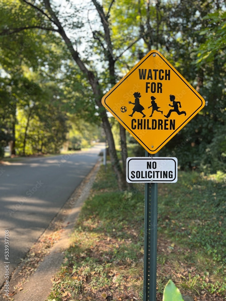 Yellow caution watch for children sign and no soliciting sign in a neighborhood with a shallow depth of field