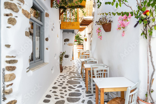 Naxos island, Cyclades Greece. Traditional outdoors cafe wooden chair table on paved street plants.