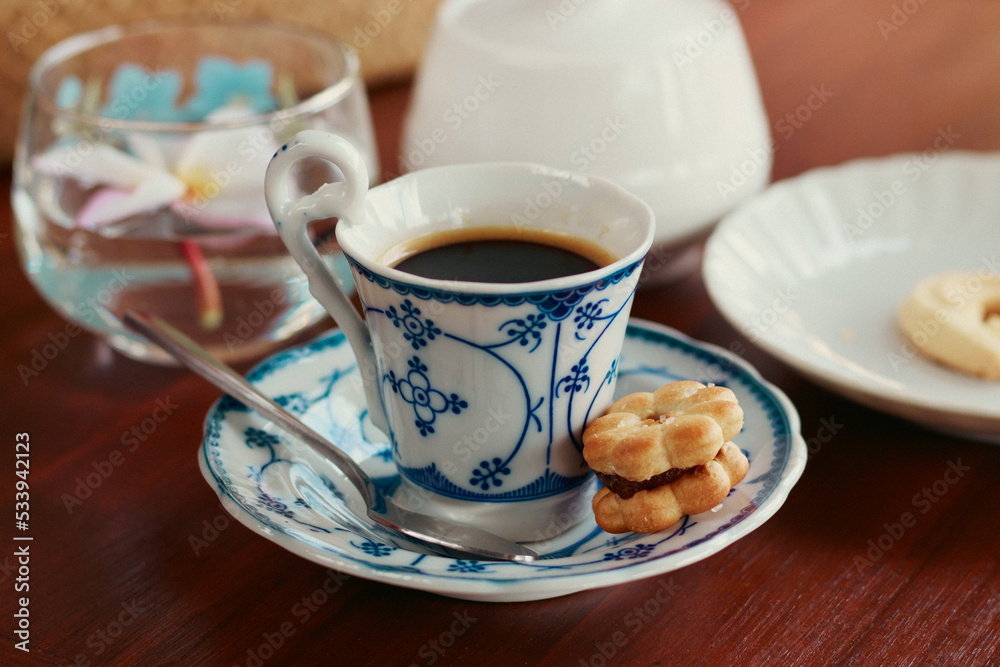 A shot of an espresso in an elegant ceramic demitasse paired with a sweet biscuit at a cafe A shot of an espresso in an elegant ceramic demitasse paired with a sweet biscuit at a cafe