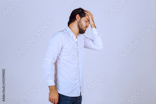 Man in white shirt coverin his face, feels sad and has headache photo