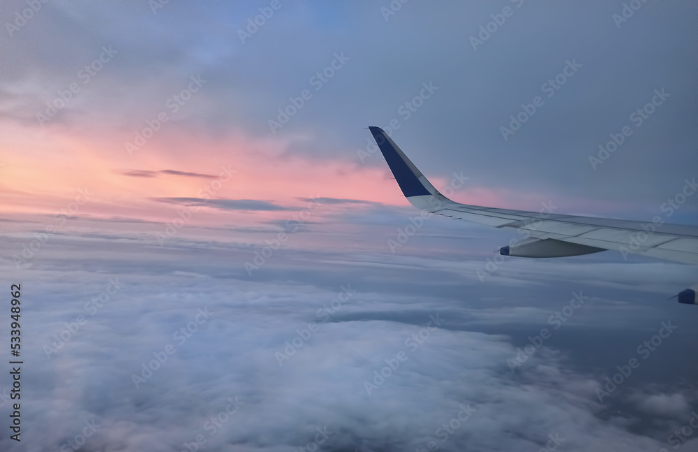 A Scenic View of the Wings of a aero plane flying above the clouds. Travelling by aero plane during sunset. - obrazy, fototapety, plakaty 
