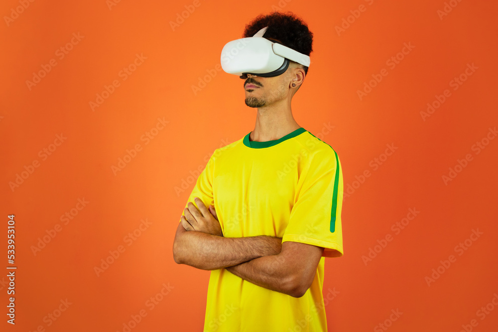 Brazilian Player - Black Man Celebrating With VR Virtual Glasses Isolated on Orange background Brazilian Player - Black Man Celebrating With VR Virtual Glasses Isolated on Orange background