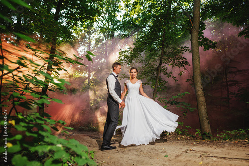 Wedding photo session. Smiling bride and groom. They stand against the backdrop of a smoky forest.