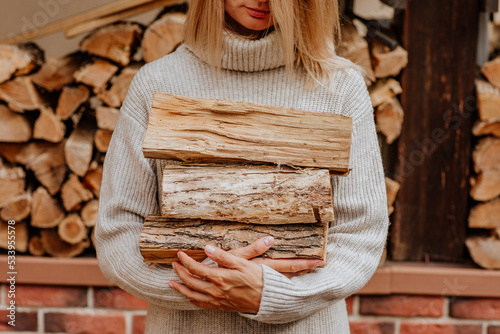 Young woman in long winter beige sweater is posing at with fire woods