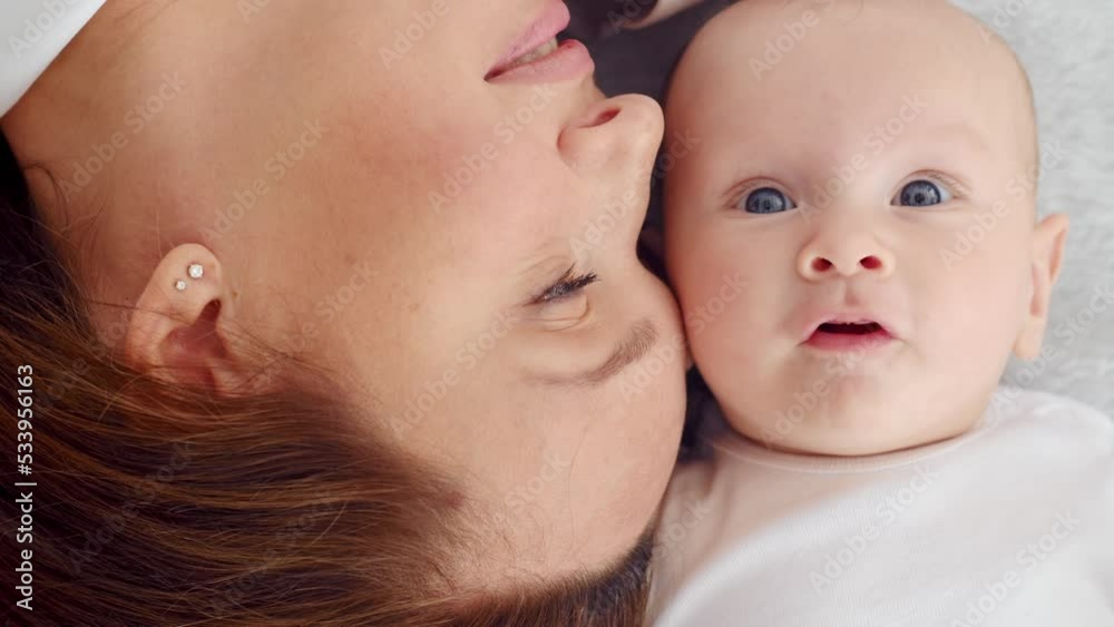 Happy newborn baby with his mother. Closeup Faces of the mother and infant baby. Healthy newborn baby in a white t-shirt with mom. Cute Infant boy and parent, top view. Slow motion. Happy family Happy newborn baby with his mother. Closeup Faces of the mother and infant baby. Healthy newborn baby in a white t-shirt with mom. Cute Infant boy and parent, top view. Slow motion. Happy family