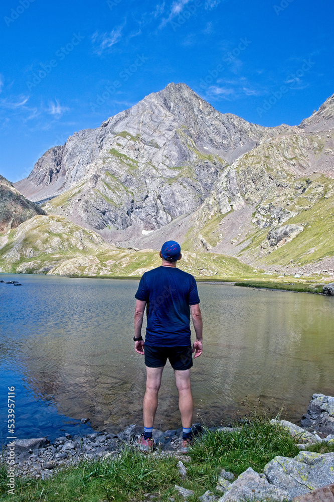 Man looking away celebrates reaching Ibon Azul Superior, a lake in the Aragon region of the Spanish Pyrenees, with Pico Piedrafita behind