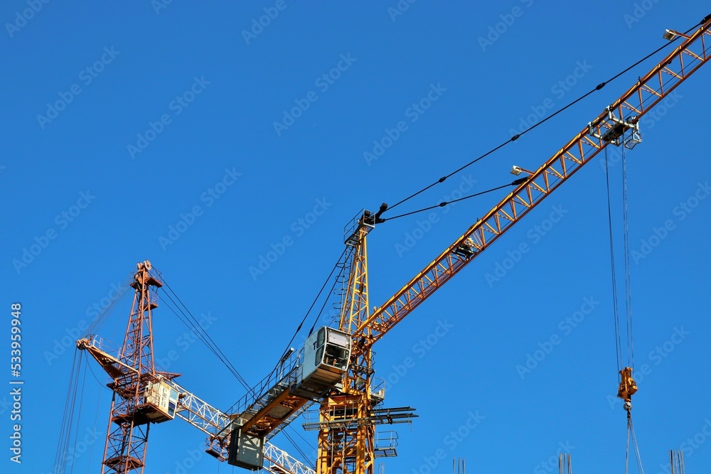 View of construction cranes and reinforced concrete houses under construction View of construction cranes and reinforced concrete houses under construction