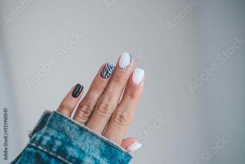 Beautiful female hands with a manicure in a denim jacket. Stylish nail design. Manicure with black and white zebra stripes on the nails. photo