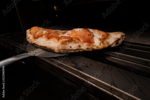 Pizza clazone saliendo del horno, lista para que los clientes coman comida hecha al estilo italiano en restaurante photo
