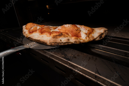 Pizza clazone saliendo del horno, lista para que los clientes coman comida hecha al estilo italiano en restaurante