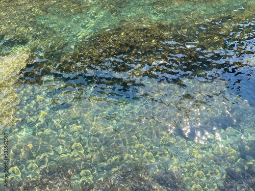 Sea emerald jade transparent water with smooth pebbles and algae at the seabed.