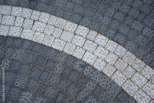 Detail of curved walkway with two different colored square cement light and dark pavers