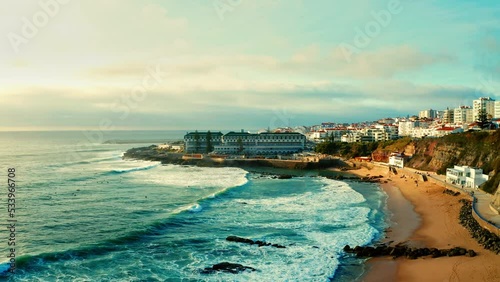 Drone view over sandy beach on summer on sunset.  Aerial view - coastline on summer while sunset.  Beautiful sunset with skyline, seashore, hotels and rolling waves. Touristic city Ericeira , Portugal