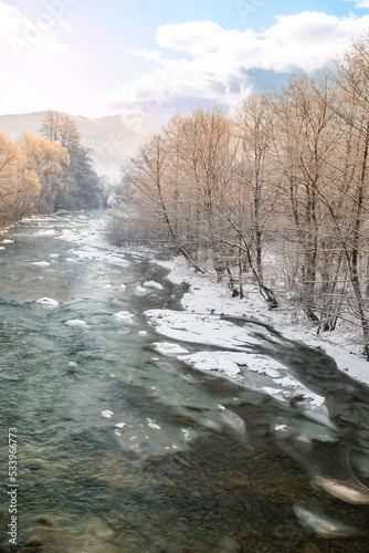 a frozen river flows near the trees in the snow on a cold winter day