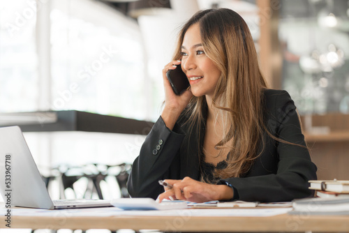 Using mobile, cheerful young asian business woman working at working place.