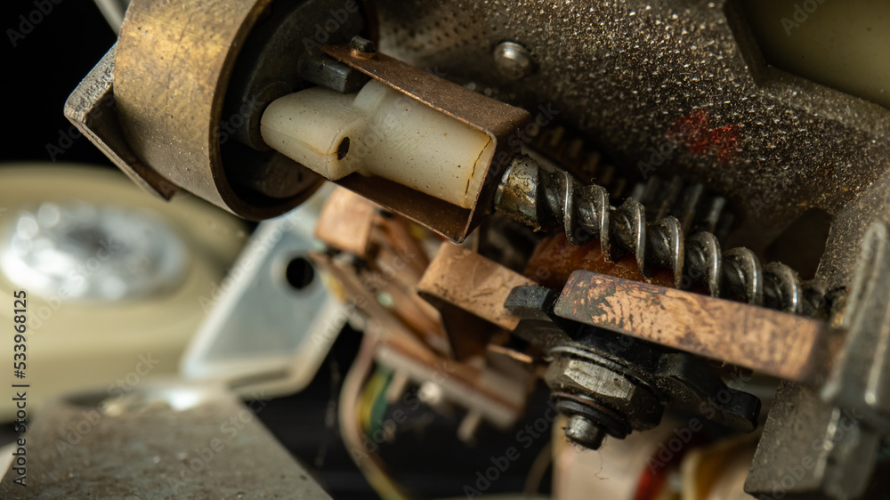 Internal mechanism of an old disassembled rotary telephone. Threaded metal screws, nuts, gears, dusty plastic parts. A macro shot of the details of a broken vintage landline phone. Repair in workshop. Internal mechanism of an old disassembled rotary telephone. Threaded metal screws, nuts, gears, dusty plastic parts. A macro shot of the details of a broken vintage landline phone. Repair in workshop.