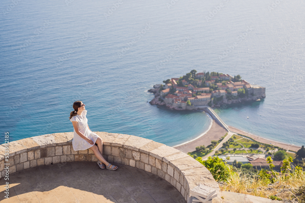 Woman tourist on background of beautiful view of the island of St. Stephen, Sveti Stefan on the Budva Riviera, Budva, Montenegro. Travel to Montenegro concept Portrait of a disgruntled girl sitting at Woman tourist on background of beautiful view of the island of St. Stephen, Sveti Stefan on the Budva Riviera, Budva, Montenegro. Travel to Montenegro concept Portrait of a disgruntled girl sitting at