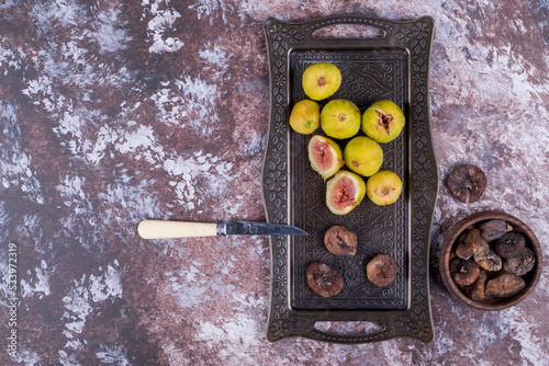Whole, dry and sliced figs in a metallic tray and in a wooden cup on the marble