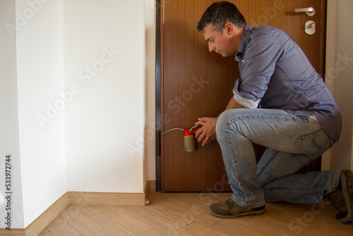 Picture of a handyman who with an oiler lubricates the hinges of a creaking door. Housework and do-it-yourself 