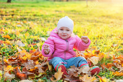 Happy young girl playing under falling yellow leaves in beautiful autumn park on nature walks outdoors. Little child throws up autumn orange maple leaves. Hello autumn concept