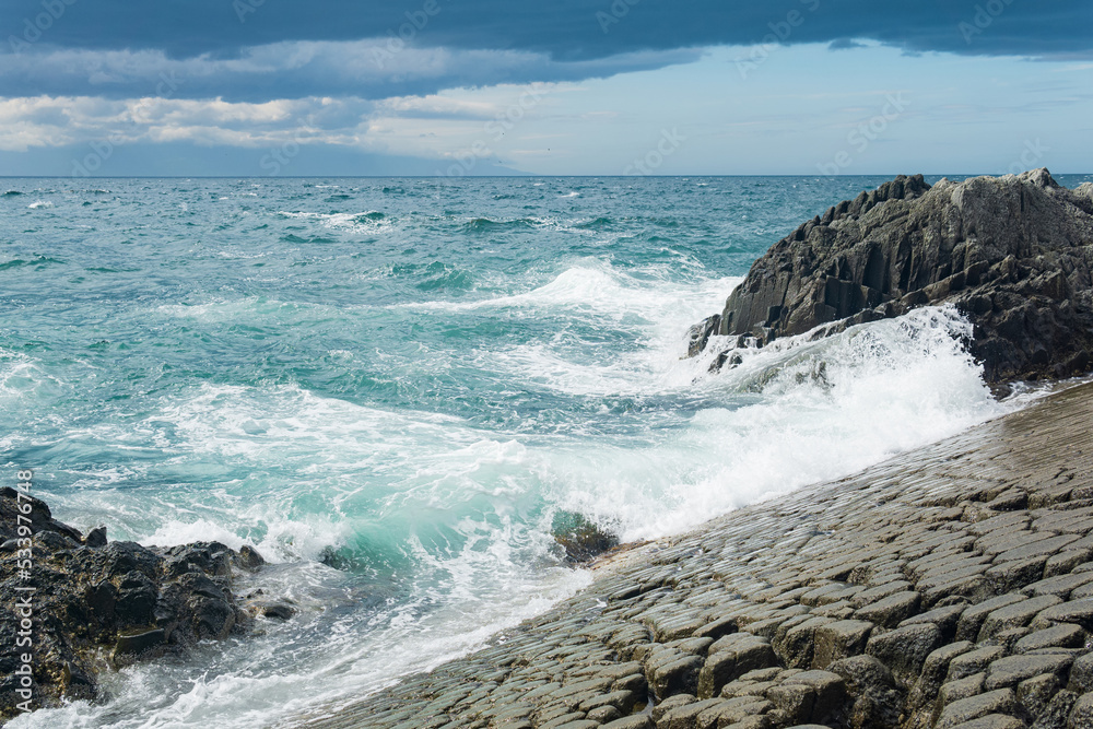 rocky seashore formed by columnar basalt against the surf, coastal landscape of the Kuril Islands